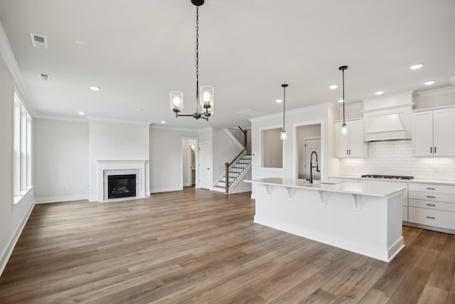 kitchen featuring a kitchen bar, custom range hood, sink, a center island with sink, and white cabinets