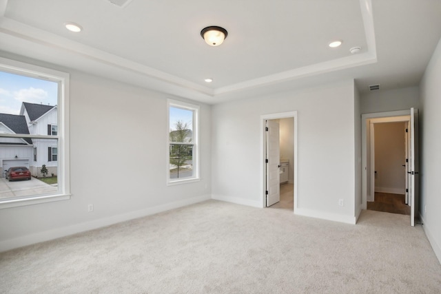 unfurnished bedroom featuring a raised ceiling, light carpet, and connected bathroom