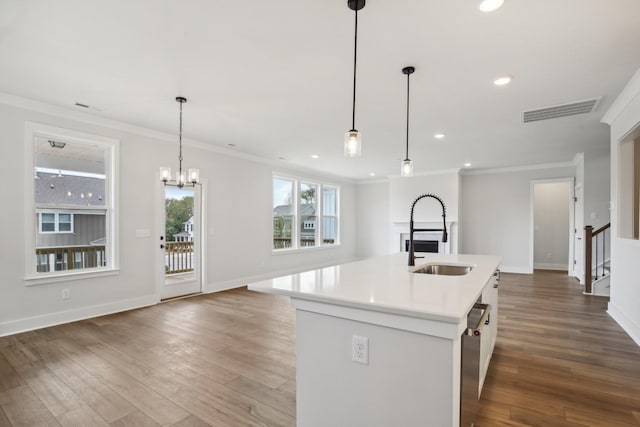 kitchen with pendant lighting, sink, ornamental molding, and a kitchen island with sink