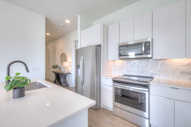 kitchen with sink, light wood-type flooring, tasteful backsplash, white cabinetry, and stainless steel appliances