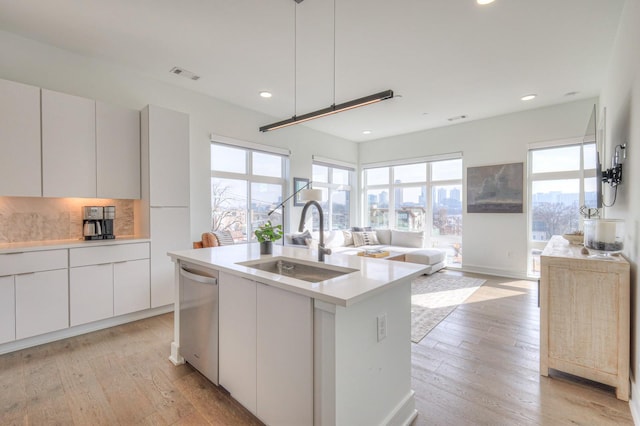 kitchen featuring white cabinets, dishwasher, sink, and an island with sink