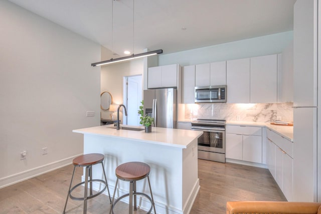 kitchen with a kitchen island with sink, sink, white cabinets, and appliances with stainless steel finishes