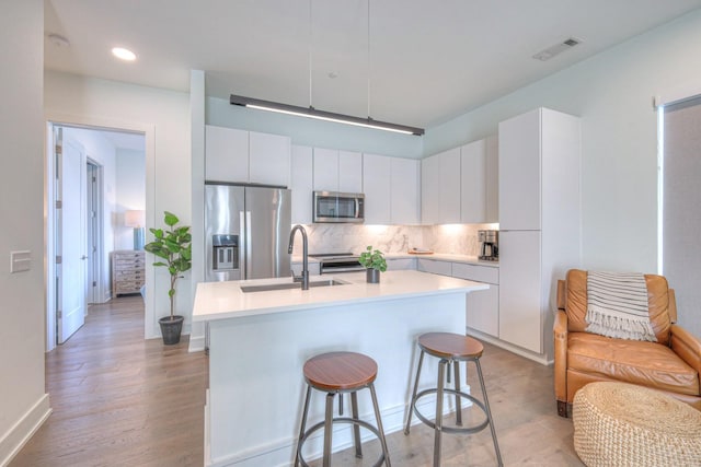 kitchen featuring white cabinetry, sink, stainless steel appliances, tasteful backsplash, and an island with sink