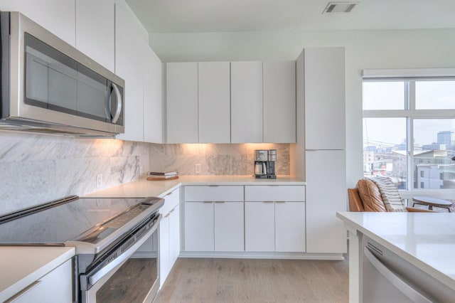 kitchen with backsplash, stainless steel appliances, white cabinetry, and light hardwood / wood-style floors