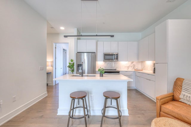 kitchen with white cabinets, stainless steel appliances, a breakfast bar area, and an island with sink