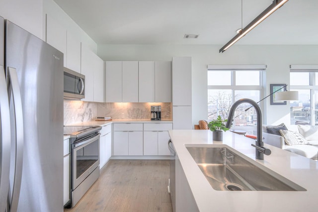 kitchen featuring appliances with stainless steel finishes, backsplash, sink, light hardwood / wood-style floors, and white cabinetry