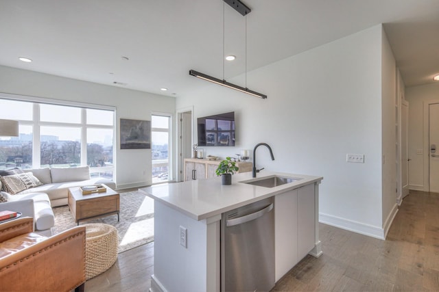 kitchen with stainless steel dishwasher, sink, a center island with sink, light hardwood / wood-style floors, and hanging light fixtures