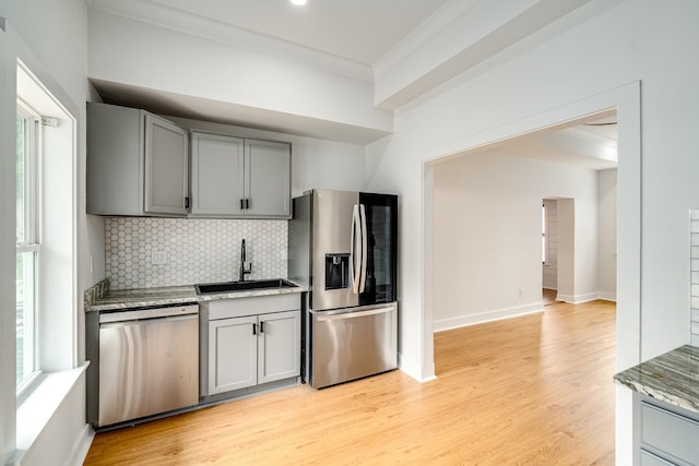 kitchen featuring decorative backsplash, light stone countertops, light wood-type flooring, stainless steel appliances, and sink