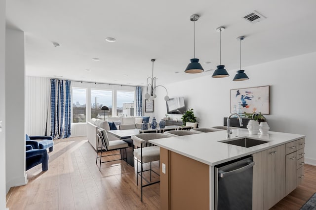 kitchen with a kitchen island with sink, sink, stainless steel dishwasher, light wood-type flooring, and decorative light fixtures