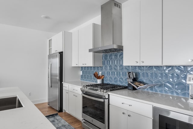 kitchen featuring appliances with stainless steel finishes, backsplash, wall chimney exhaust hood, white cabinets, and hardwood / wood-style floors