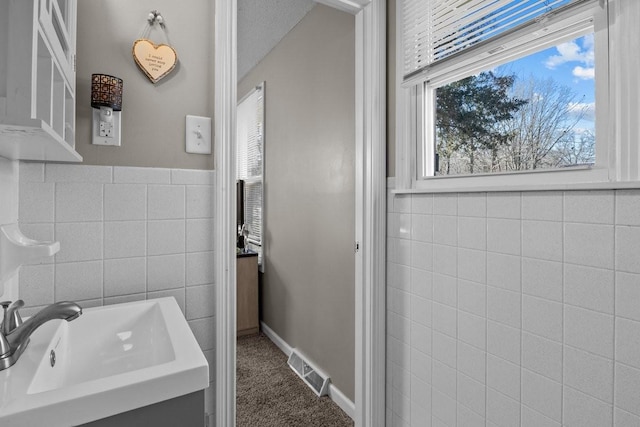 bathroom featuring a textured ceiling, a healthy amount of sunlight, sink, and tile walls