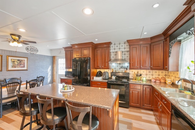 kitchen with black appliances, a kitchen breakfast bar, wall chimney range hood, sink, and a kitchen island