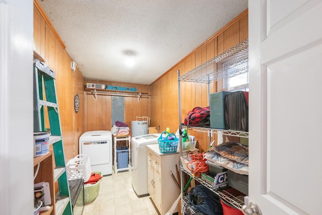 clothes washing area with washing machine and dryer, wood walls, a textured ceiling, and electric water heater