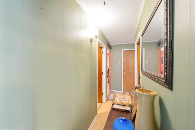 hallway featuring a textured ceiling, light hardwood / wood-style floors, crown molding, and wooden walls