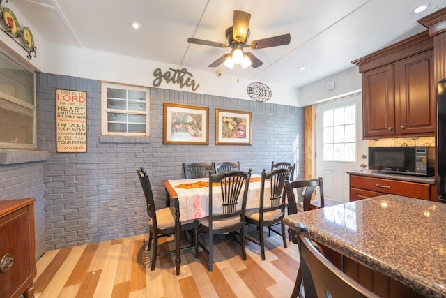 dining area featuring ceiling fan, light wood-type flooring, and brick wall