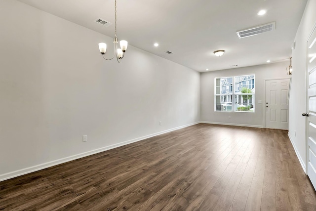 spare room featuring dark wood-type flooring and a notable chandelier