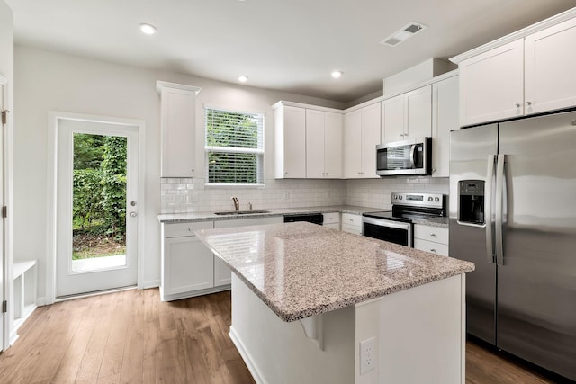 kitchen featuring light stone countertops, appliances with stainless steel finishes, light hardwood / wood-style flooring, white cabinets, and a kitchen island