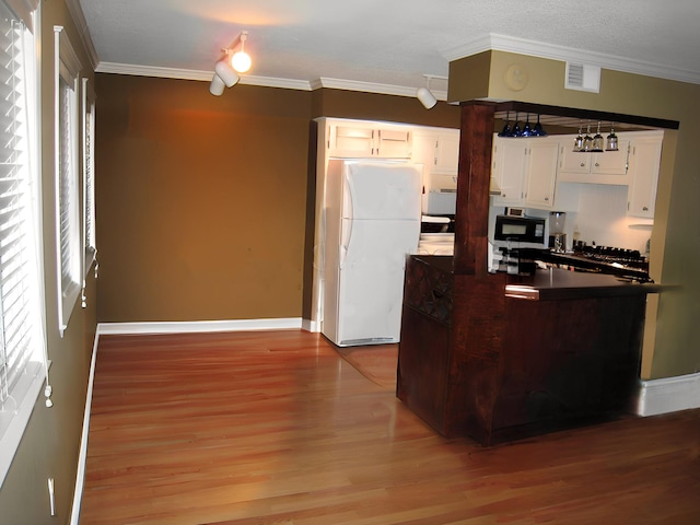 kitchen featuring white refrigerator, ornamental molding, and white cabinets