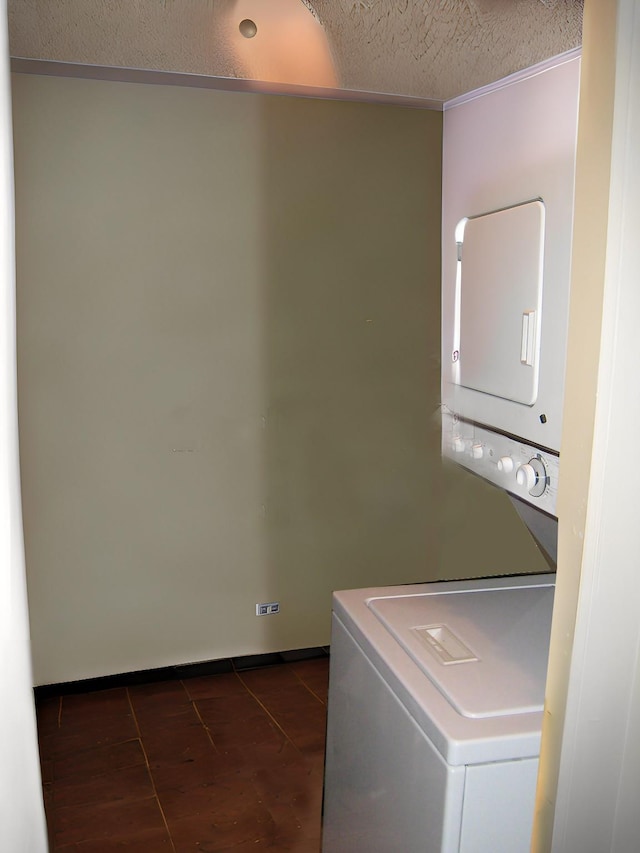 washroom with stacked washer and dryer, dark tile patterned flooring, and a textured ceiling