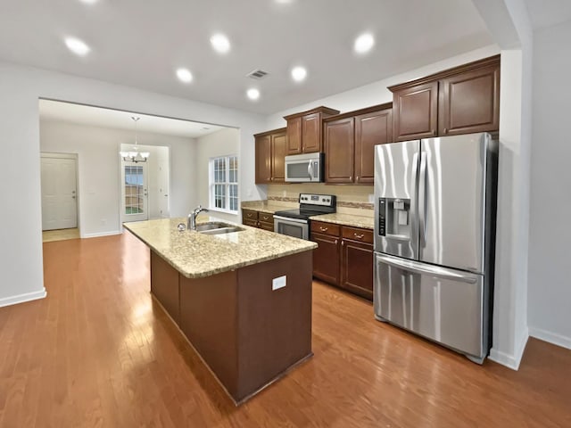 kitchen with sink, stainless steel appliances, an inviting chandelier, an island with sink, and hardwood / wood-style flooring