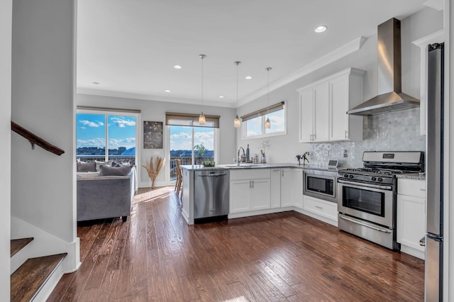 kitchen featuring white cabinetry, stainless steel appliances, wall chimney range hood, and decorative light fixtures