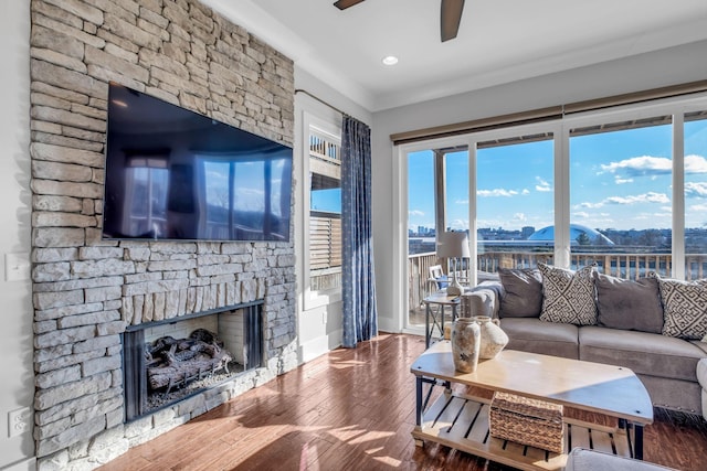 living room featuring hardwood / wood-style flooring, ceiling fan, a stone fireplace, and crown molding