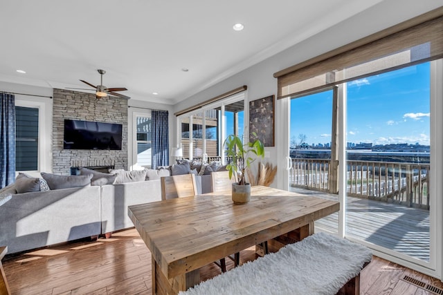 dining space featuring ceiling fan, a stone fireplace, crown molding, a water view, and hardwood / wood-style flooring