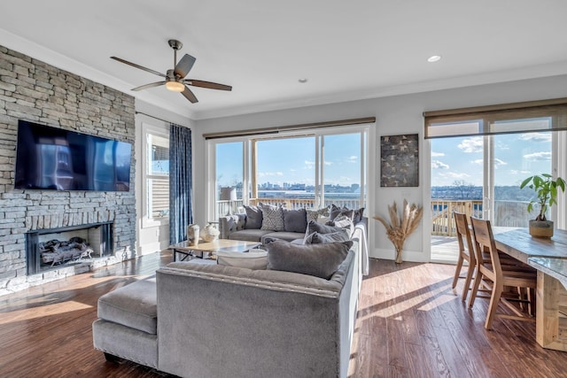 living room featuring a stone fireplace, crown molding, hardwood / wood-style floors, and a wealth of natural light