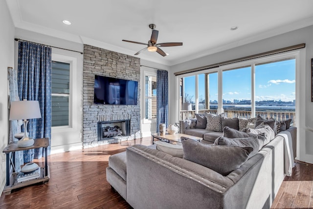 living room with ceiling fan, dark hardwood / wood-style flooring, a stone fireplace, and crown molding