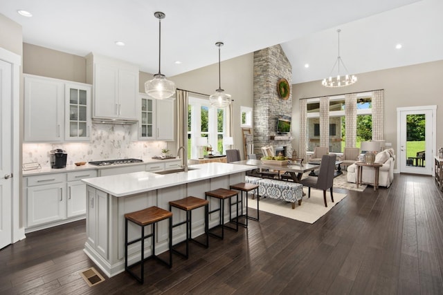 kitchen with tasteful backsplash, white cabinetry, sink, and a center island with sink