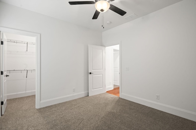 unfurnished bedroom with carpet, ceiling fan, a spacious closet, and a closet