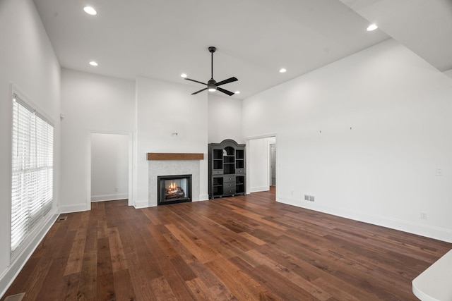 unfurnished living room featuring ceiling fan, dark hardwood / wood-style flooring, and a high ceiling