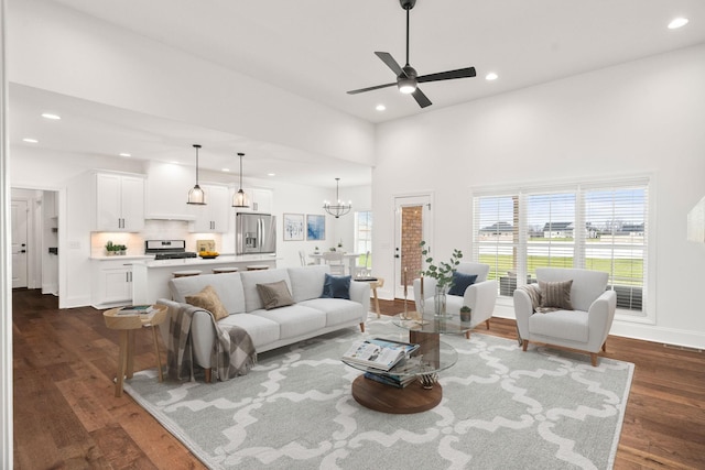 living room featuring dark hardwood / wood-style floors, ceiling fan with notable chandelier, a wealth of natural light, and a high ceiling