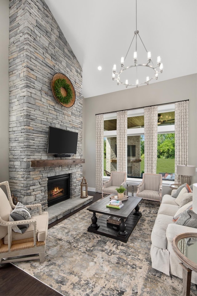 living room featuring wood-type flooring, high vaulted ceiling, a stone fireplace, and a notable chandelier