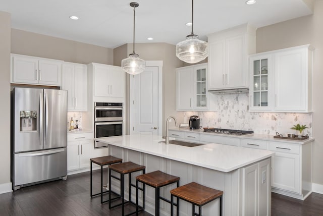 kitchen with stainless steel appliances, a kitchen island with sink, sink, white cabinetry, and hanging light fixtures