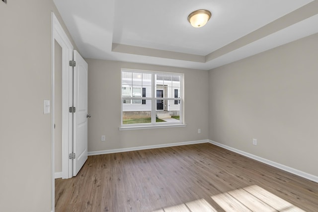 spare room featuring a tray ceiling and light hardwood / wood-style floors