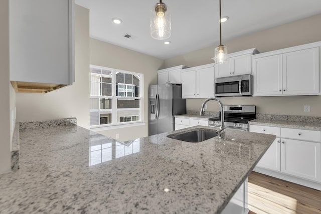 kitchen with white cabinetry, sink, hanging light fixtures, light stone counters, and appliances with stainless steel finishes