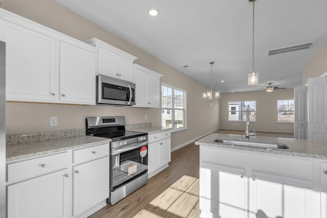 kitchen featuring light stone countertops, white cabinetry, sink, stainless steel appliances, and ceiling fan with notable chandelier