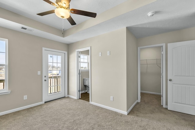 unfurnished bedroom with light colored carpet, a raised ceiling, ceiling fan, a spacious closet, and a closet