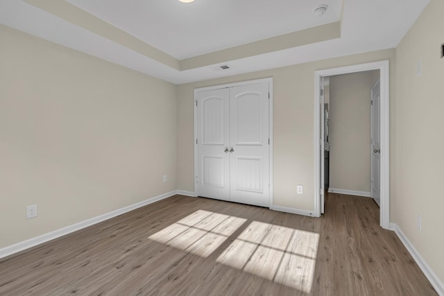 unfurnished bedroom featuring a tray ceiling, a closet, and light wood-type flooring