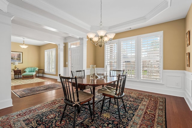 dining room featuring dark wood-type flooring, an inviting chandelier, decorative columns, a tray ceiling, and ornamental molding