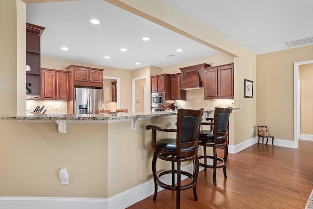 kitchen featuring a kitchen bar, appliances with stainless steel finishes, kitchen peninsula, tasteful backsplash, and premium range hood