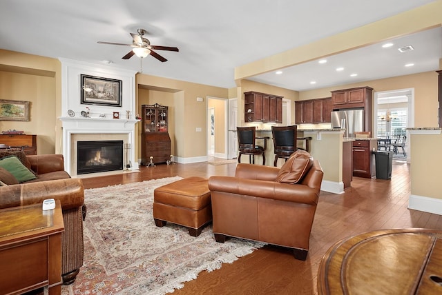 living room featuring ceiling fan, a fireplace, and dark wood-type flooring