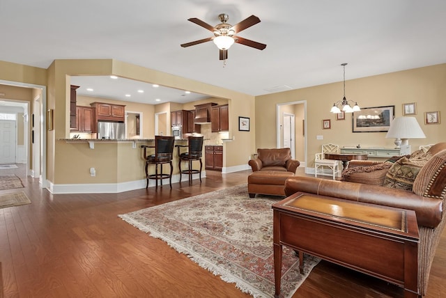 living room with ceiling fan with notable chandelier and dark wood-type flooring