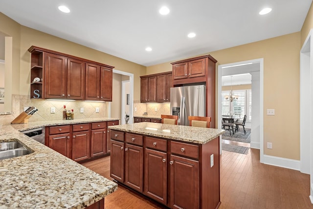 kitchen featuring a center island, an inviting chandelier, hardwood / wood-style flooring, light stone counters, and stainless steel fridge with ice dispenser