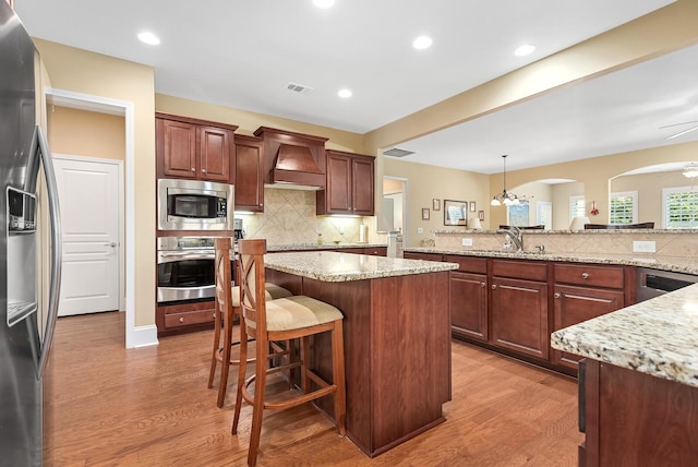 kitchen featuring appliances with stainless steel finishes, tasteful backsplash, premium range hood, hardwood / wood-style flooring, and hanging light fixtures