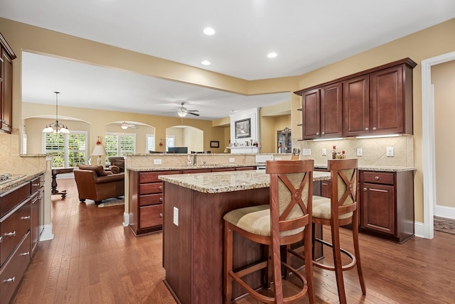 kitchen with a kitchen breakfast bar, dark hardwood / wood-style floors, decorative backsplash, decorative light fixtures, and kitchen peninsula