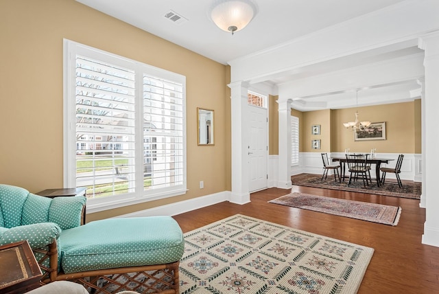 sitting room with a chandelier, ornate columns, and dark wood-type flooring