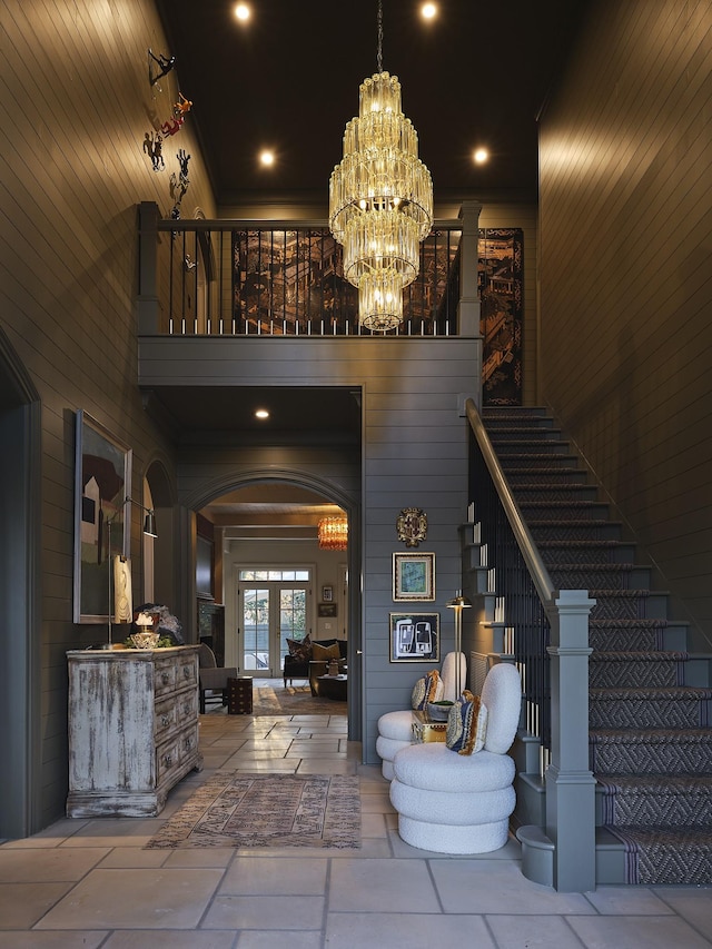 foyer featuring a towering ceiling, an inviting chandelier, and wooden walls