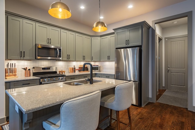 kitchen with dark wood-type flooring, sink, hanging light fixtures, light stone countertops, and appliances with stainless steel finishes